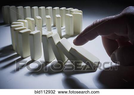 Stock Image - Hispanic man knocking over dominoes. Fotosearch