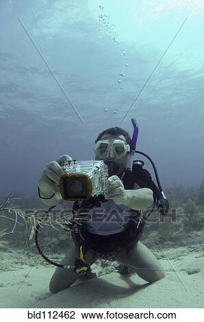 Stock Image - Hispanic scuba diver taking pictures underwater. Fotosearch