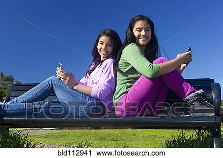 Hispanic teenage girls sitting on park bench View Large Photo Image Stock Image - Hispanic teenage girls sitting on park bench. Fotosearch