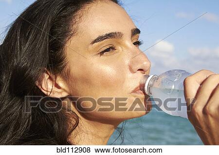 Hispanic woman drinking water bottle on beach View Large Photo Image Stock Photo - Hispanic woman drinking water bottle on beach. Fotosearch