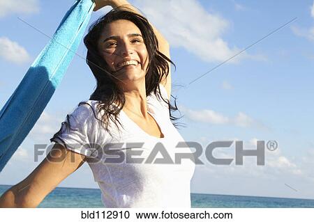 Stock Image - Hispanic woman playing with towel on beach. Fotosearch