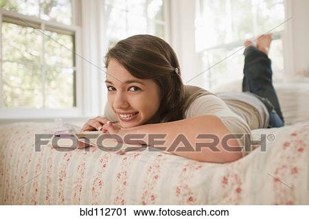 Stock Image - Mixed race girl laying in bed writing in journal. Fotosearch