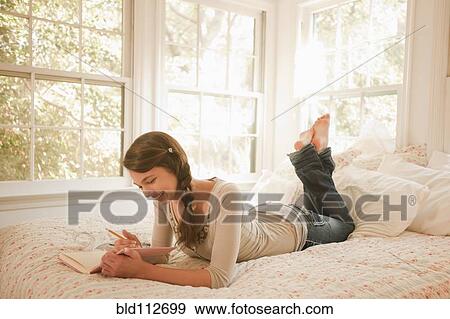 Stock Photo - Mixed race girl laying in bed writing in journal. Fotosearch
