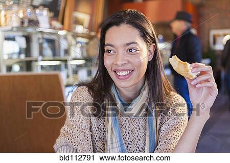 Stock Image - Mixed race woman eating in coffee shop. Fotosearch