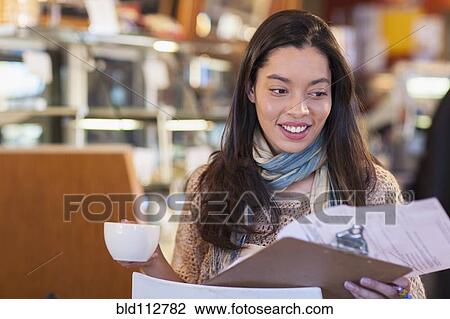 Stock Image - Mixed race woman reading clipboard in coffee shop. Fotosearch