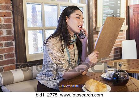 Stock Photography - Mixed race woman reading menu in cafe. Fotosearch