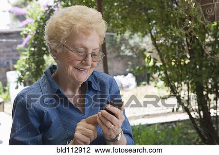 Stock Image - Older Hispanic woman using cell phone outdoors. Fotosearch