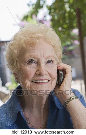 Stock Image - Older Hispanic woman using cell phone outdoors. Fotosearch