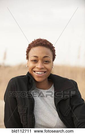 Stock Image - Smiling African American woman sitting outdoors. Fotosearch