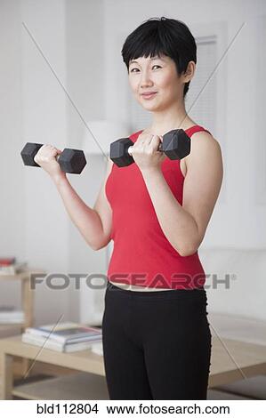 Woman lifting weights in living room View Large Photo Image Picture - Woman lifting weights in living room. Fotosearch