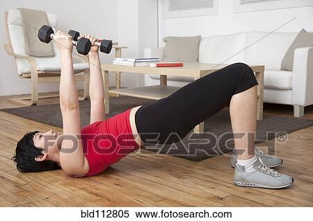 Stock Photography - Woman lifting weights in living room. Fotosearch