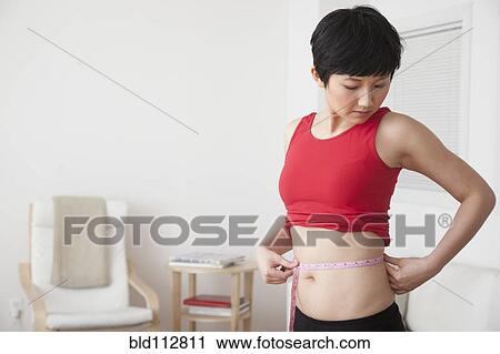 Woman measuring her waist in living room View Large Photo Image Stock Image - Woman measuring her waist in living room. Fotosearch