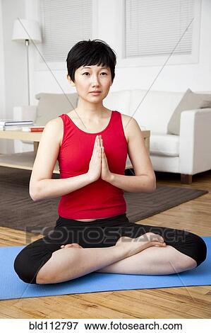 Stock Photo - Woman meditating in living room. Fotosearch