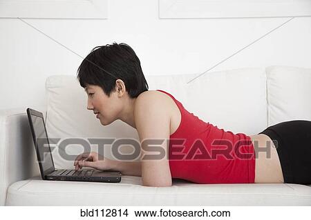 Picture - Woman using laptop on sofa in living room. Fotosearch