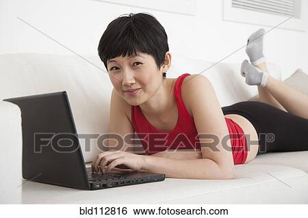 Stock Photograph - Woman using laptop on sofa in living room. Fotosearch