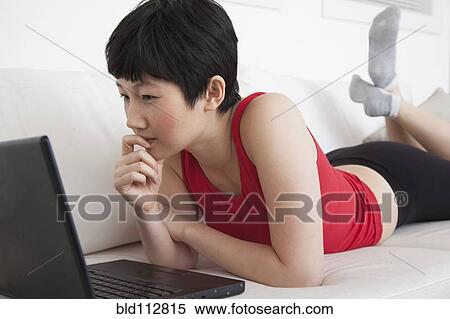 Stock Photography - Woman using laptop on sofa in living room. Fotosearch