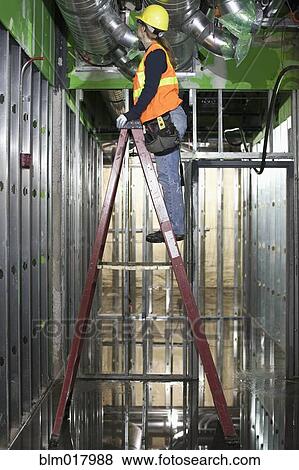 Stock Photo - African American worker climbing ladder on site. Fotosearch