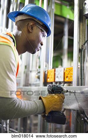 Picture - African American worker drilling metal on site. Fotosearch