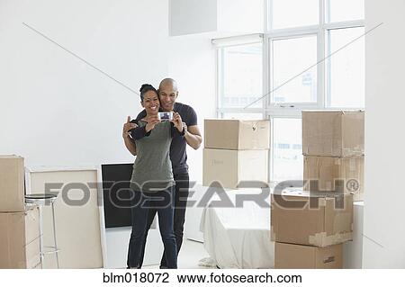 Stock Image - Black couple using cell phone in new house. Fotosearch