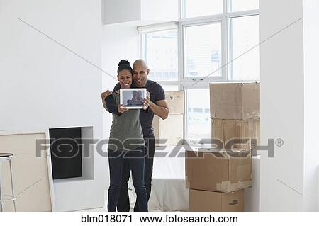 Stock Image - Black couple using tablet computer in new house. Fotosearch