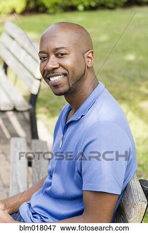 Stock Photo - Black man smiling on park bench. Fotosearch
