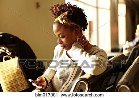 Stock Image - Black woman using cell phone in airport. Fotosearch