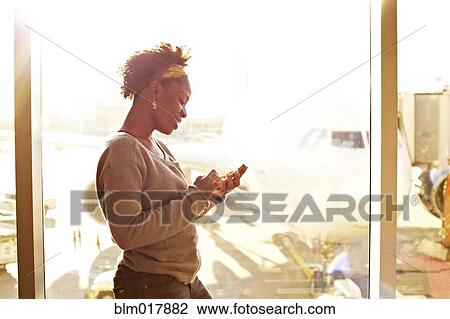 Stock Image - Black woman using cell phone in airport. Fotosearch