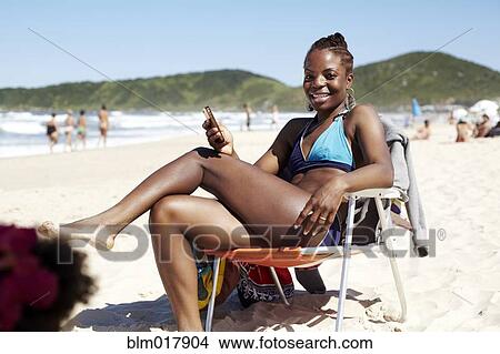Picture - Black woman using cell phone on beach. Fotosearch