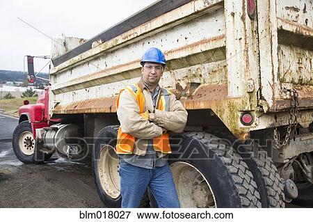 Caucasian worker standing by truck on site View Large Photo Image Stock Photo - Caucasian worker standing by truck on site. Fotosearch