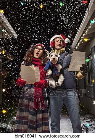 Stock Image - Couple singing Christmas carols with dog. Fotosearch