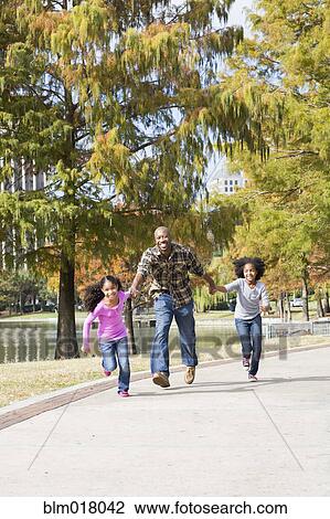 Stock Image - Father and daughters playing in park. Fotosearch