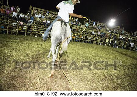 Stock Image - Hispanic cowboy riding horse in rodeo. Fotosearch