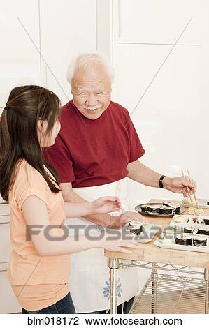 Stock Image - Japanese man and granddaughter cooking in kitchen. Fotosearch