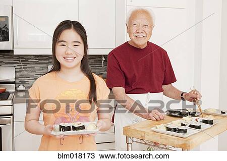 Stock Image - Japanese man and granddaughter cooking in kitchen. Fotosearch