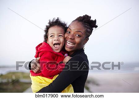 Stock Image - Mother holding daughter on beach. Fotosearch