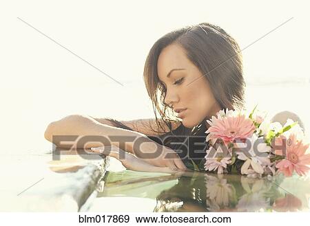 Stock Photo - Pacific Islander woman holding flowers in pool. Fotosearch