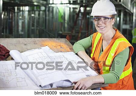 Stock Photo - Woman reading blueprints on construction site. Fotosearch