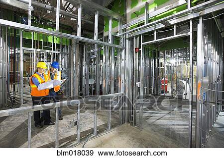 Stock Photo - Workers reading blueprints on site. Fotosearch