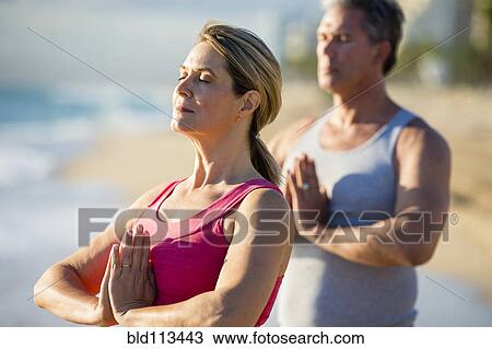 Stock Image - Caucasian couple meditating on beach. Fotosearch