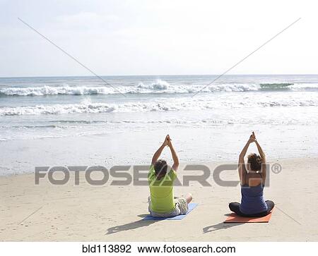 Stock Image - Caucasian couple meditating on beach. Fotosearch