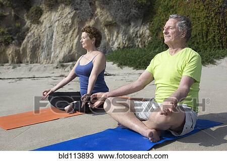 Stock Image - Caucasian couple meditating on beach. Fotosearch
