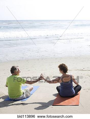 Stock Photograph - Caucasian couple practicing yoga on beach. Fotosearch