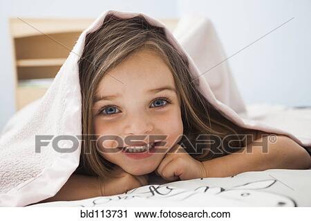 Stock Image - Caucasian girl smiling under covers. Fotosearch