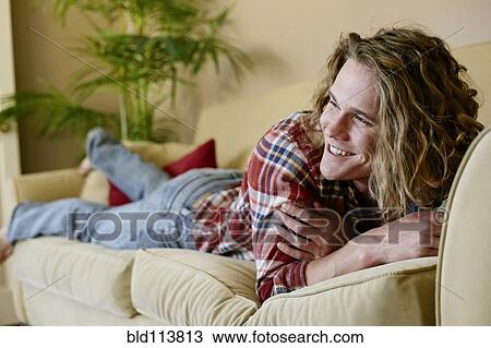 Stock Image - Caucasian man laying on sofa. Fotosearch