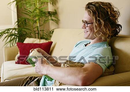 Stock Image - Caucasian man reading on sofa. Fotosearch