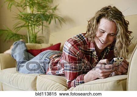 Stock Photography - Caucasian man using cell phone on sofa. Fotosearch