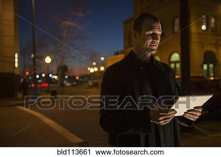 Stock Image - Caucasian man using tablet computer on city street. Fotosearch