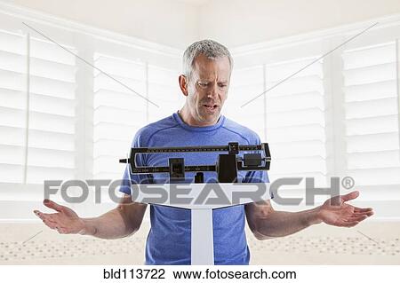 Stock Image - Caucasian man weighing himself. Fotosearch
