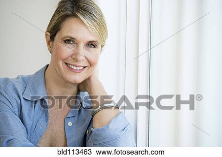 Stock Image - Caucasian woman smiling in window. Fotosearch