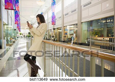 Stock Photo - Caucasian woman using cell phone in shopping mall. Fotosearch